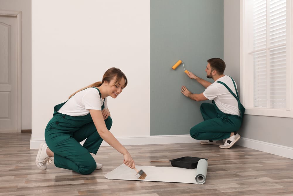 Two renovation workers painting and preparing an interior wall with rollers and brushes during a remodeling project – home renovations st louis mo