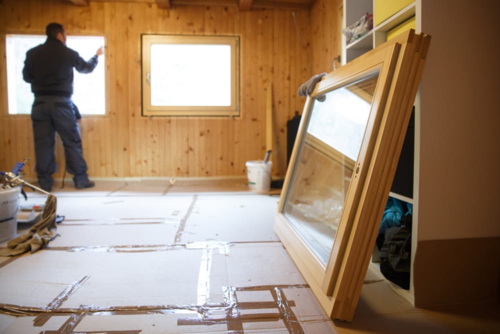 New wooden window frames resting on the floor while a worker prepares an opening for installation in a wood-paneled room – Window Installation Springfield MO